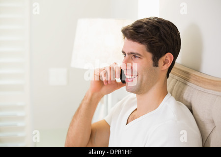 Casual Uomo sorridente con il cellulare a letto Foto Stock