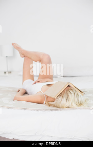 Giovane donna con libro sulla faccia appoggiata a letto Foto Stock