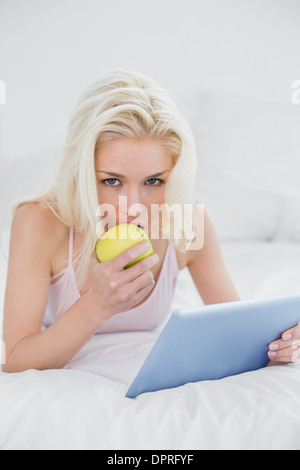 Casual giovane biondo con tablet PC una mela a letto Foto Stock