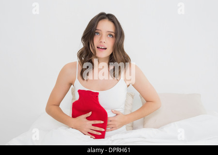 Donna con acqua calda sacca di gomma su stomaco a letto Foto Stock