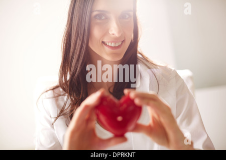 Immagine della donna sorridente con cuore rosso in mani guardando la fotocamera Foto Stock