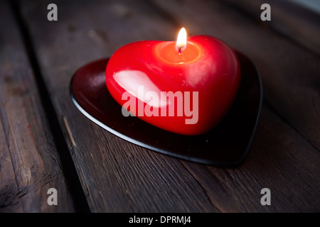 Immagine di colore rosso a forma di cuore la masterizzazione di candela su sfondo di legno Foto Stock