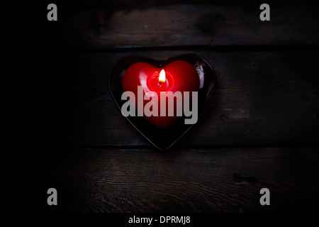 Immagine di colore rosso a forma di cuore la masterizzazione di candela su sfondo di legno Foto Stock