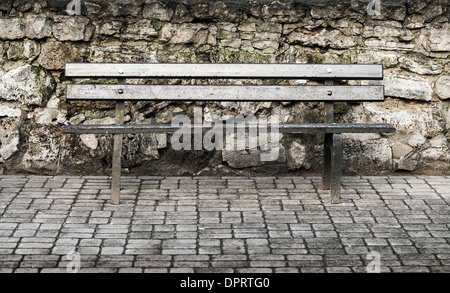 Panca in legno vicino a vecchio muro di pietra nel parco Foto Stock