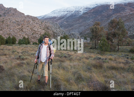 Uomo con zaino e bastoncini da trekking a piedi sul paesaggio Foto Stock