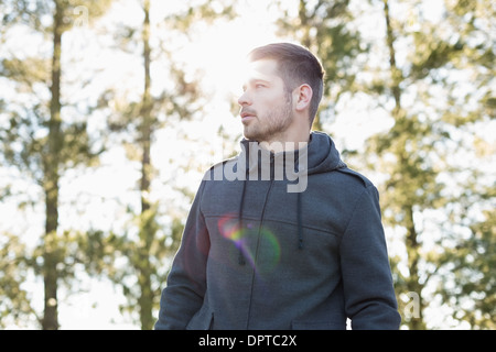 Uomo in pullover in piedi nella foresta contro alberi Foto Stock