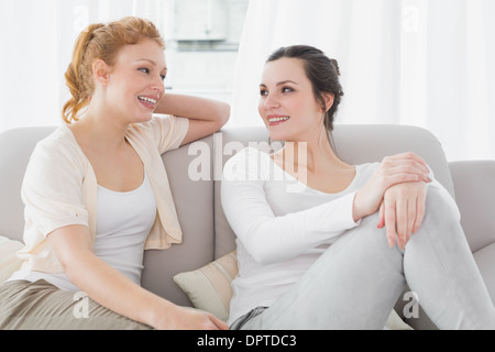 Due femmina sorridente amici seduti sul divano nel soggiorno Foto Stock