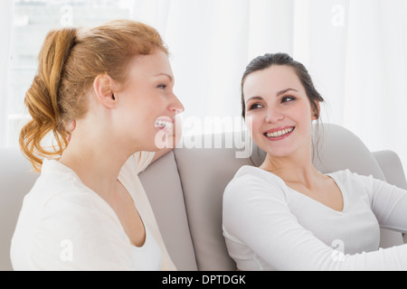 Due femmina sorridente amici seduti sul divano nel soggiorno Foto Stock