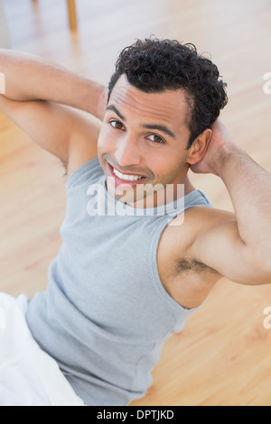 Uomo sorridente facendo sgranocchia addominale nel soggiorno Foto Stock