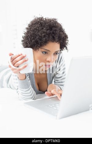 Grave donna con tazza da caffè utilizzando laptop a letto Foto Stock