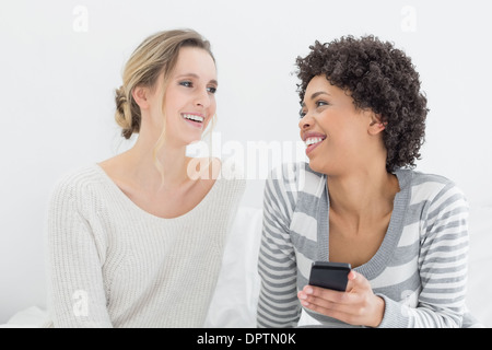 Donna sorridente amici la lettura di un messaggio di testo sul letto Foto Stock