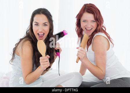 Allegro giovane femmina amici cantando in spazzole per capelli Foto Stock