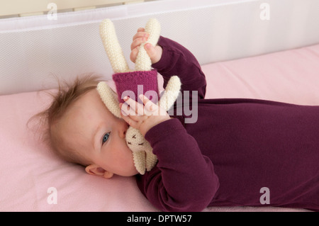 Bambina che giace nella sua culla e giocare con un giocattolo morbido Foto Stock