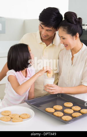 Ragazza godendo di biscotti e latte con i genitori in cucina Foto Stock