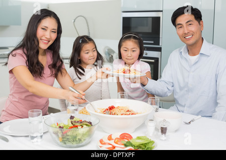 La famiglia felice di quattro godendo di spaghetti pranzo in lui cucina Foto Stock