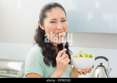 Vista laterale ritratto di una donna di mangiare insalata in cucina Foto Stock