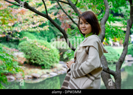 Ritratto di giovane donna sorridente in telecamera in un parco di fronte a un lago Foto Stock