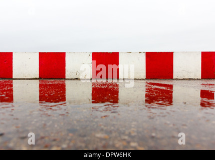 Rosso bianco parete in calcestruzzo sull'asfalto umido Foto Stock