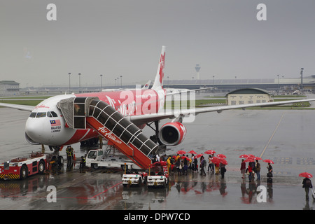 Imbarco passeggeri Air Asia airlines volo utilizzando la scala nella pioggia, con ombrelloni rosso fornito dalla compagnia aerea Foto Stock