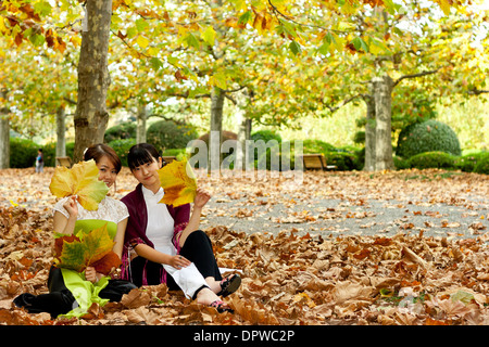 Due giovani donne in tradizionale abito vietnamita seduta in autunno lascia tenere in su grandi foglie Foto Stock