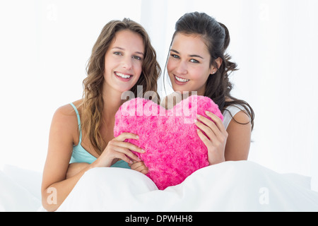 Donna sorridente amici con cuore Cuscino sagomato a letto Foto Stock