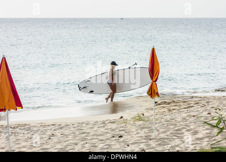 Una giovane donna in un due pezzi costume da bagno porta il suo Stand Up Paddle board fuori del Mare dei Caraibi e sulla spiaggia. Foto Stock