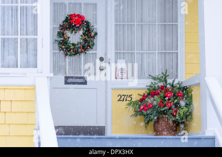 Ghirlanda di Natale e impianto sulla veranda mentre la neve cade a. Foto Stock