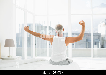 Vista posteriore di un uomo maturo stretching le sue braccia a letto Foto Stock