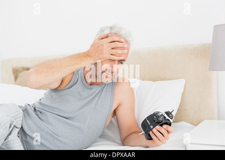 Uomo che guarda la sveglia nel letto Foto Stock