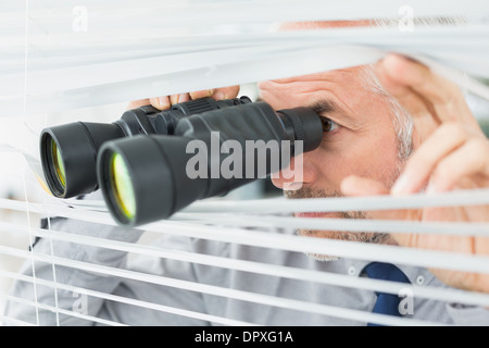 Imprenditore matura spiata con un binocolo attraverso persiane Foto Stock