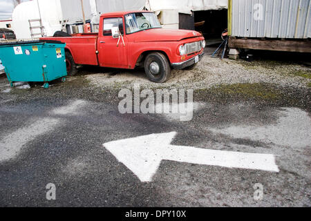 Dic 29, 2008 - Port Townsend, Washington, Stati Uniti d'America - nel cantiere navale nel porto Wownsend, WA., vecchie auto lungo le strade di tutto il mondo, compreso questo vecchio carrello giù un vicolo di via accanto a un cestino blu dumbster con un dipinto di bianco freccia traffico verniciato su asfalto a terra. (Credito Immagine: © Steven Karl Metzer/ZUMA Press) Foto Stock