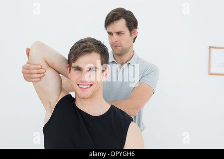 Fisioterapista maschio esaminando un sorridente mans braccio Foto Stock
