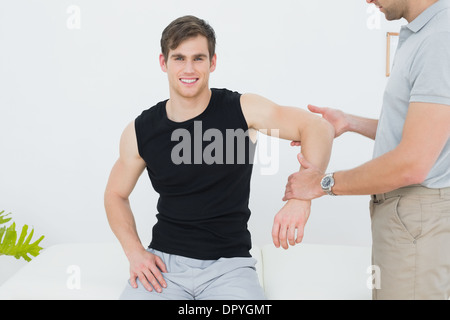 Fisioterapista maschio esaminando un sorridente mans mano Foto Stock