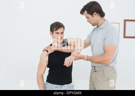 Fisioterapista maschio esaminando un giovane mans braccio Foto Stock