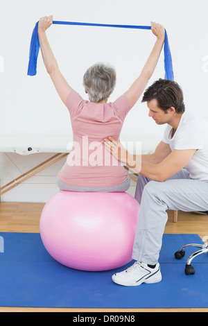 Senior donna sulla sfera di yoga con un terapista fisico Foto Stock