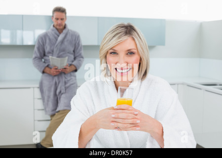 Donna con arancia e uomo che legge il giornale in cucina Foto Stock