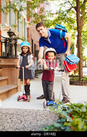 Padre tenendo i bambini su scooter a scuola Foto Stock