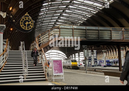 Interno del trainshed con ferro e il tetto in vetro fisso, treni & donna a piedi dalla piattaforma orologio - La stazione ferroviaria di York, North Yorkshire, Inghilterra, Regno Unito Foto Stock