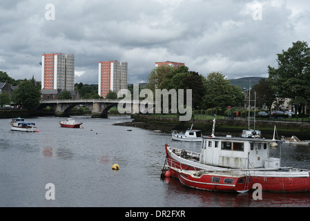 In barca sul fiume con un ponte e i blocchi di appartamenti in background. Il fiume è chiamato il fiume Leven Foto Stock