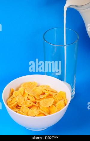 Prima colazione da versare il latte e cornflakes su sfondo blu Foto Stock