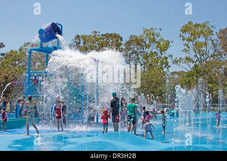 La Folla di adulti e bambini che giocano in acqua & getting intrisa come acqua e suggerimenti da sovraccarico enorme benna a Hervey Bay water park Foto Stock