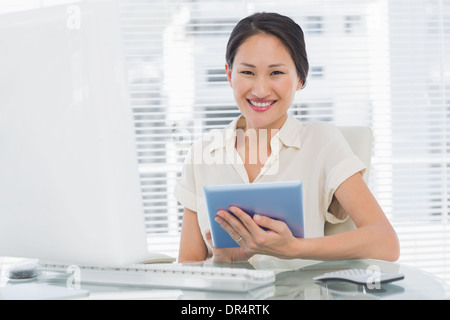 Imprenditrice sorridente con tavoletta digitale alla scrivania Foto Stock