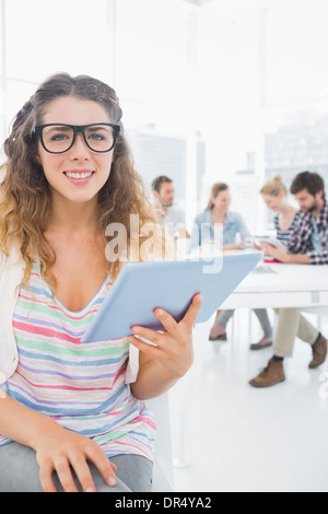 Donna con tavoletta digitale con i colleghi in background in ufficio Foto Stock