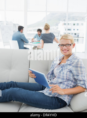 Donna con tavoletta digitale con i colleghi in background in ufficio creativo Foto Stock