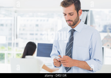 Casuale artista maschio per la messaggistica di testo con il collega in background Foto Stock