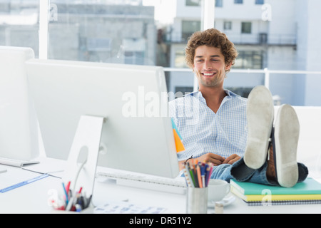 Casual giovane uomo con le gambe sulla scrivania in ufficio luminoso Foto Stock