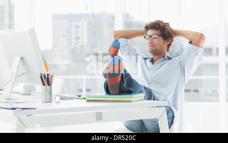 Casual giovane uomo con le gambe sulla scrivania in ufficio Foto Stock