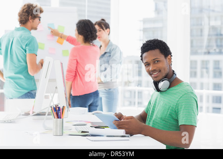 Uomo informale con tavoletta digitale con i colleghi dietro in ufficio Foto Stock