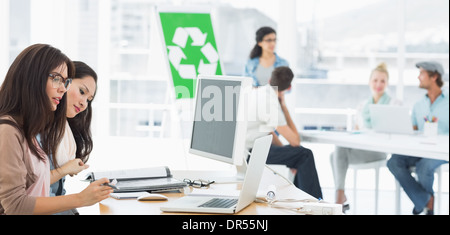 Gli artisti lavorano a scrivanie con segno di riciclaggio in background in ufficio Foto Stock