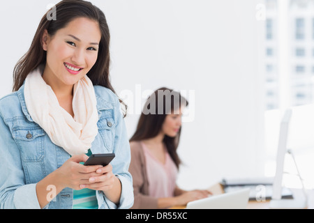 Sorridente giovane donna alla messaggistica di testo di Office Foto Stock